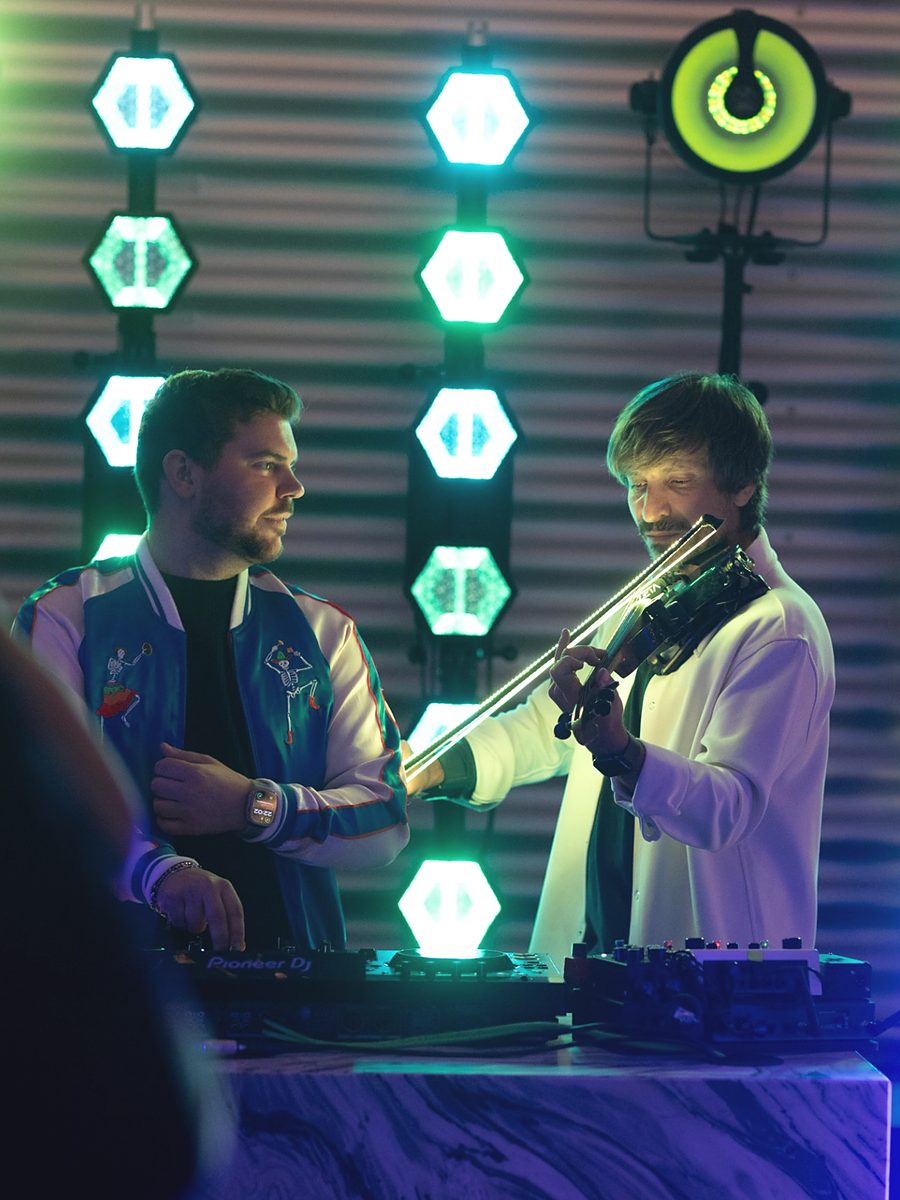 Violinista e DJ sul palco davanti a una parete di luci esagonali